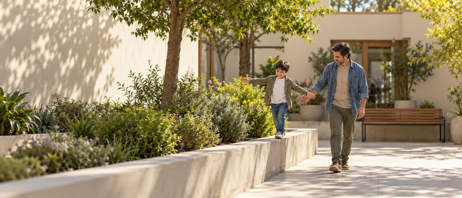 Un niño camina en equilibrio sobre un muro bajo de un jardín, tomado de la mano de su padre.